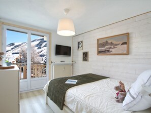A bedroom with a bed, a television, a painting, and a view of a snowy landscape through a sliding door. - Cozy duplex, near slopes - 8 guests (Les Deux Alpes)