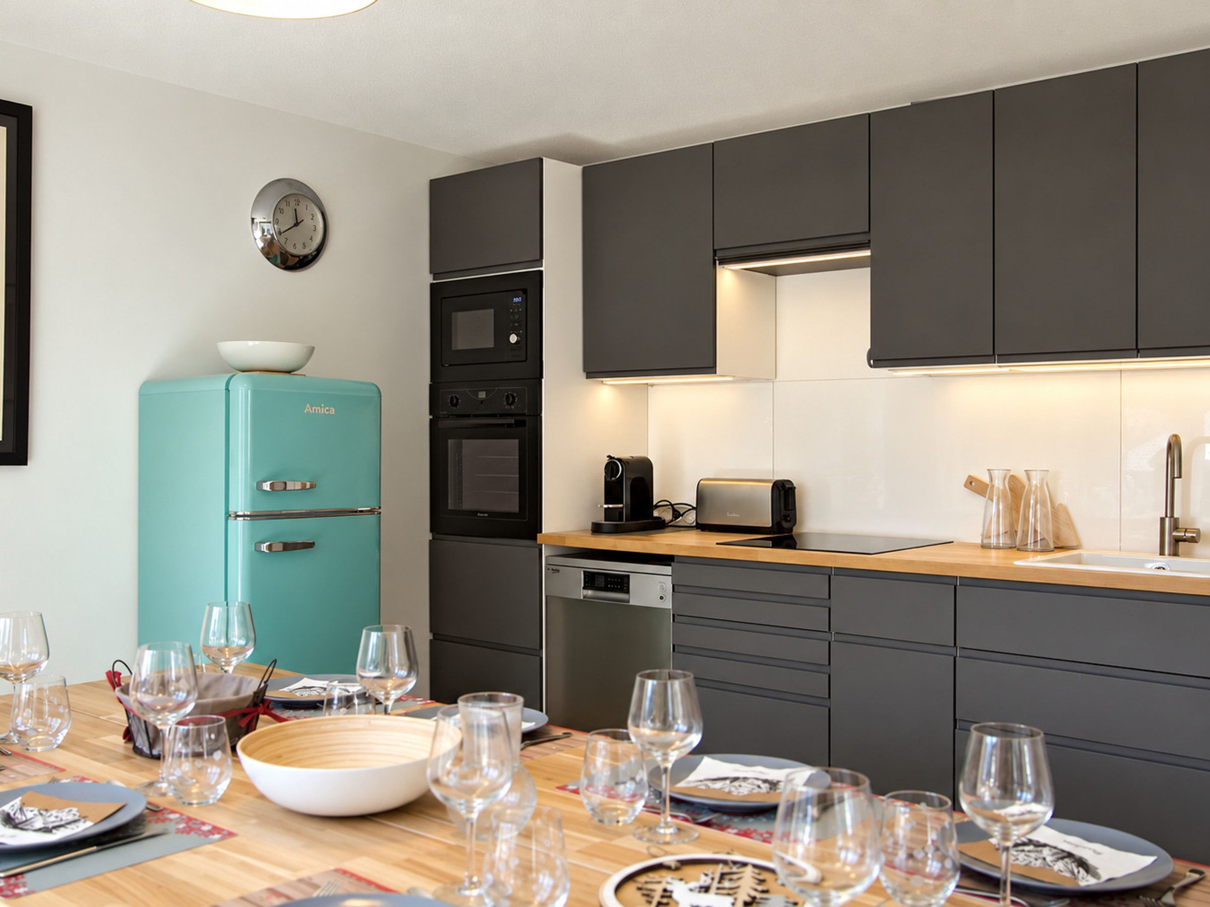 Une cuisine moderne avec un réfrigérateur de couleur turquoise, un four encastré et un micro-ondes.