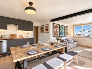 A modern kitchen with dark cabinets, a wooden dining table set for six, and a large window with a view of a snowy landscape. - Cozy duplex, near slopes - 8 guests (Les Deux Alpes)