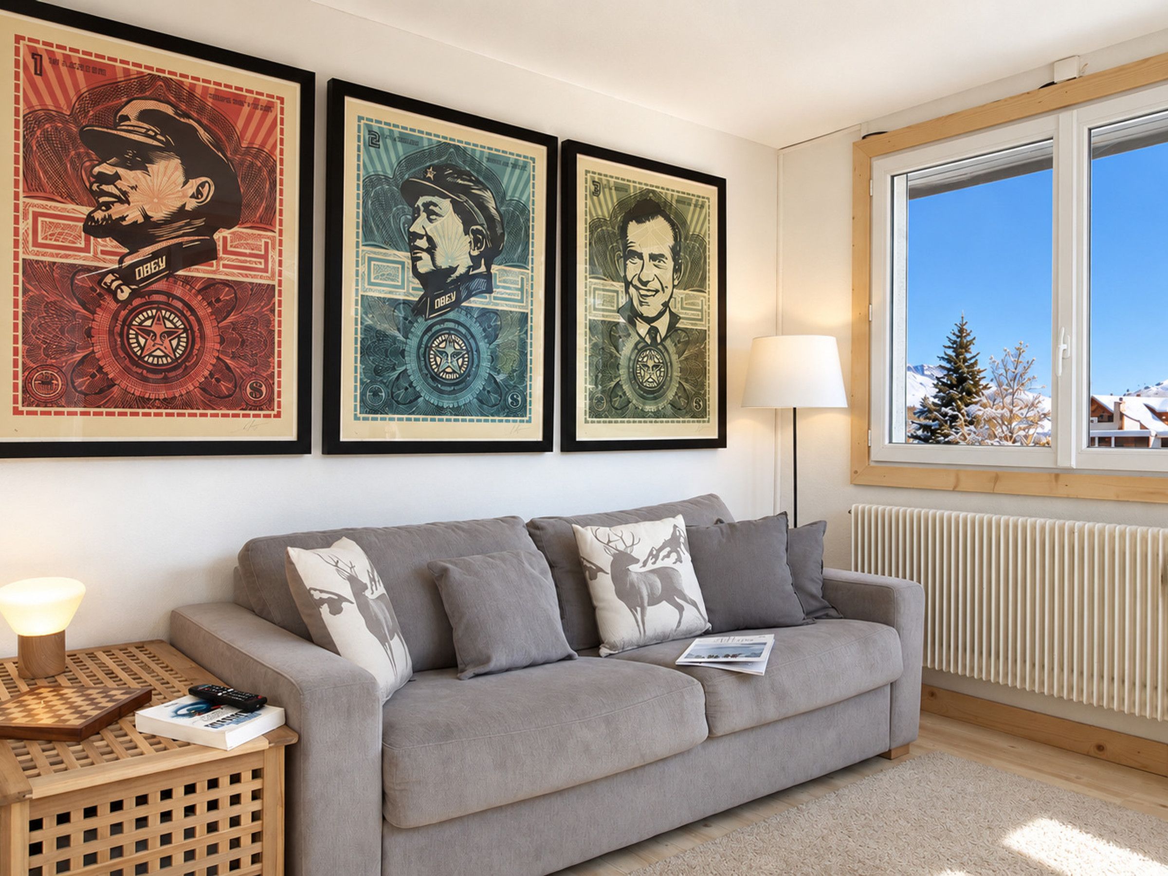 Un salon avec un canapé gris, une table d’appoint en bois sur laquelle se trouve une lampe, et trois tableaux encadrés accrochés au mur.
