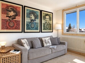 A living room with a grey sofa, a wooden side table with a lamp, and three framed pictures on the wall. - Cozy duplex, near slopes - 8 guests (Les Deux Alpes)