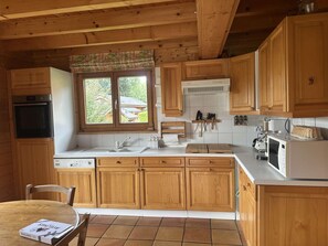 A wooden cabin kitchen with a dishwasher, oven, and a window with a view of a house.