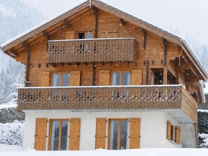 Eine zweistöckige Holzhütte mit Balkon, großen Fenstern und einem mit Schnee bedeckten Dach.