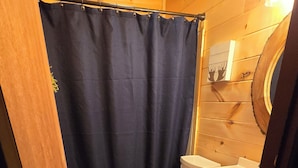 Une petite salle de bain comprenant des toilettes, un meuble en bois, un rideau de douche et un luminaire.