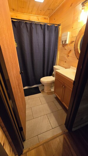 Een kleine badkamer met toilet, een houten kastje, een douchegordijn en een lamp.