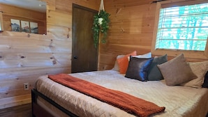 Une chambre à coucher avec un lit, des murs en bois, un ventilateur de plafond et une fenêtre avec des stores.