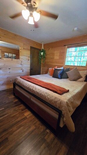 Een slaapkamer met een bed, houten wanden, een plafondventilator en een raam met zonwering.