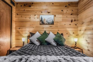 A bedroom with a wooden paneled wall, a bed with a grey quilt, and a picture of a forest. - Your Home Away From Home 3 bedrooms, 2 bathrooms, 7 minutes to Pigeon Forge (Sevierville)