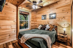 A wooden cabin bedroom with a bed, a window, a ceiling fan, and two wall-mounted pictures. - Your Home Away From Home 3 bedrooms, 2 bathrooms, 7 minutes to Pigeon Forge (Sevierville)
