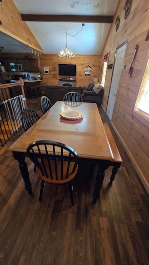 Een houten interieur met een eettafel, stoelen, een televisie en een keukenhoek.