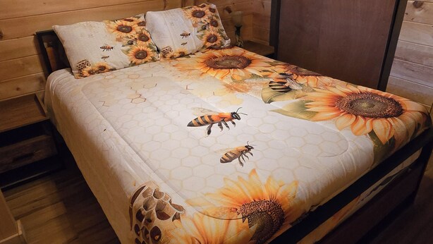 Une chambre dans un chalet en bois, avec un lit agrémenté d’une couvre-lit aux motifs floraux et d’abeilles.