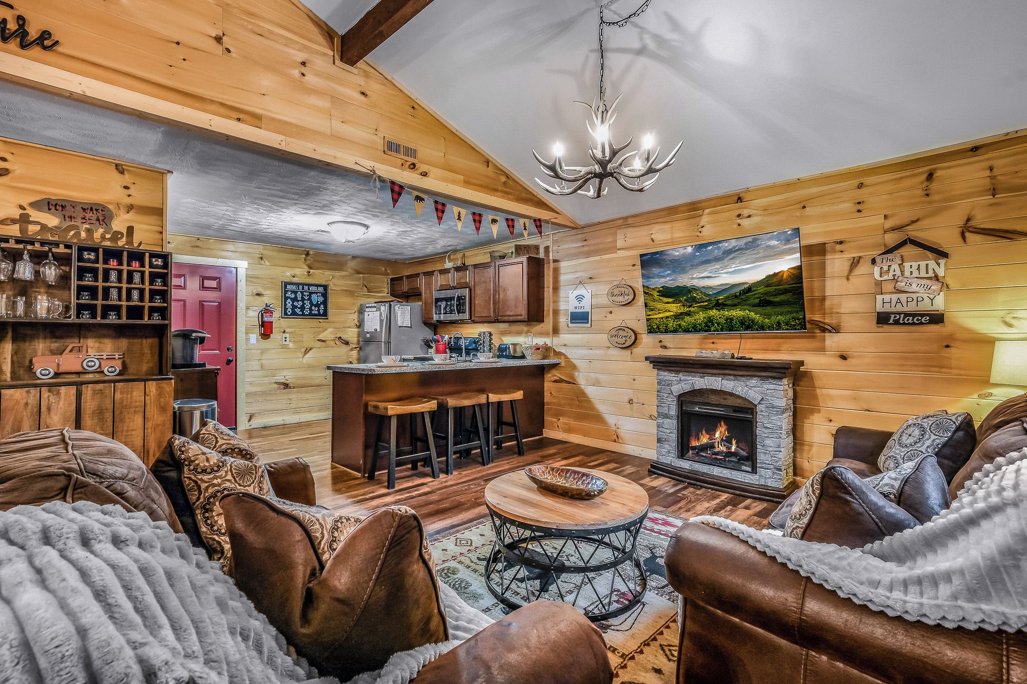 L’intérieur chaleureux d’un chalet avec une cheminée, des murs en bois, un coin cuisine et un espace salon doté de canapés en cuir.