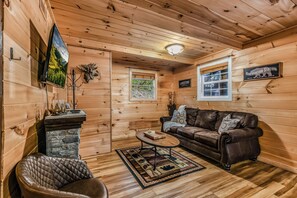 A cozy cabin interior with a stone fireplace, a leather sofa, a coffee table, and wooden walls. - Your Home Away From Home 3 bedrooms, 2 bathrooms, 7 minutes to Pigeon Forge (Sevierville)