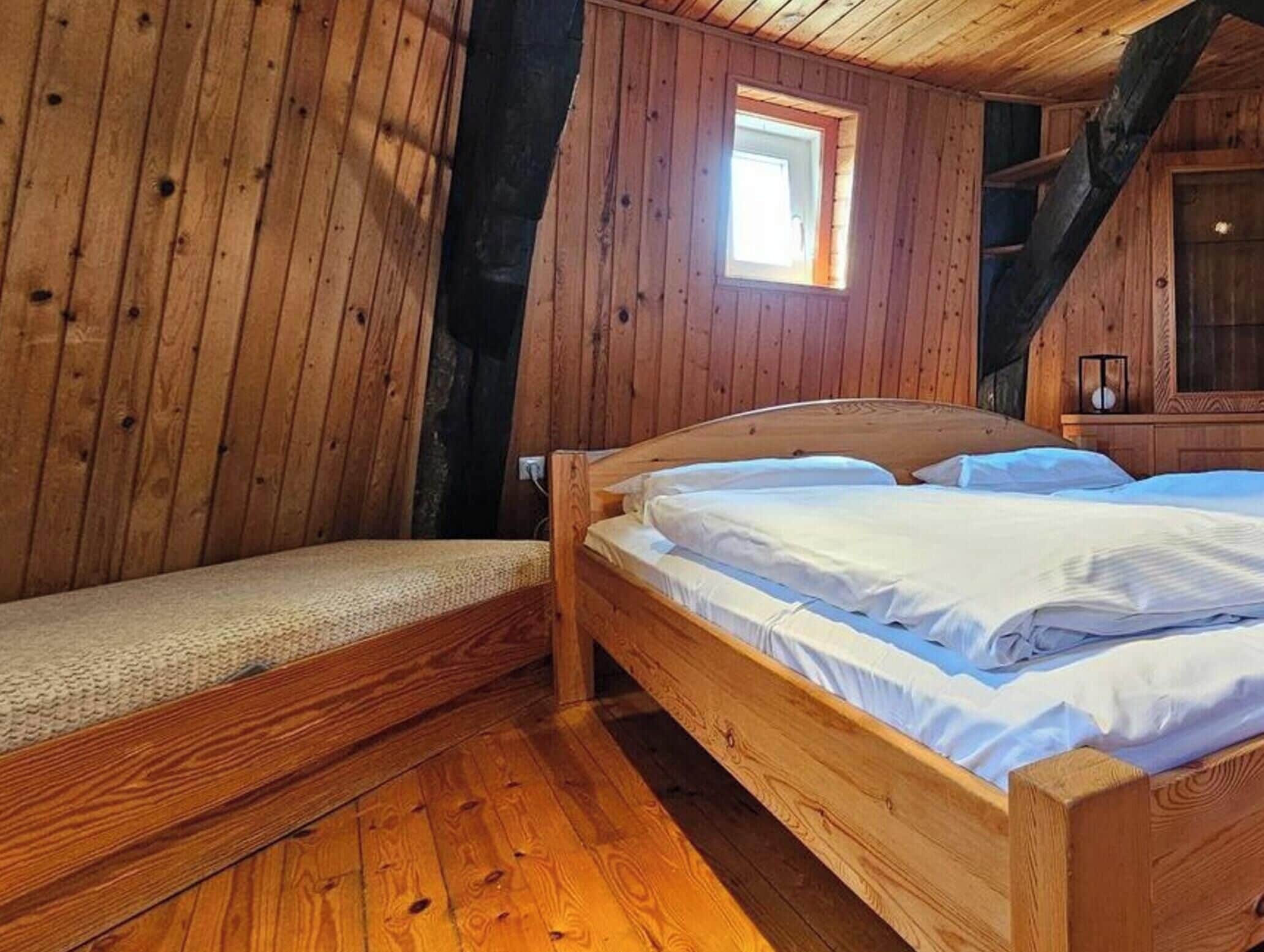 A wooden cabin room with a bed, a bench, and a small window.