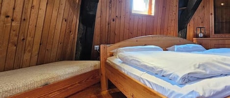 A wooden cabin room with a bed, a bench, and a small window.