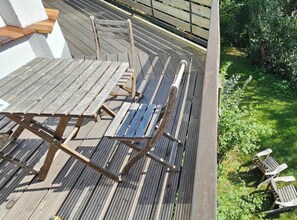Eine Holzterrasse mit Tisch und Stühlen, umgeben von viel Grün.