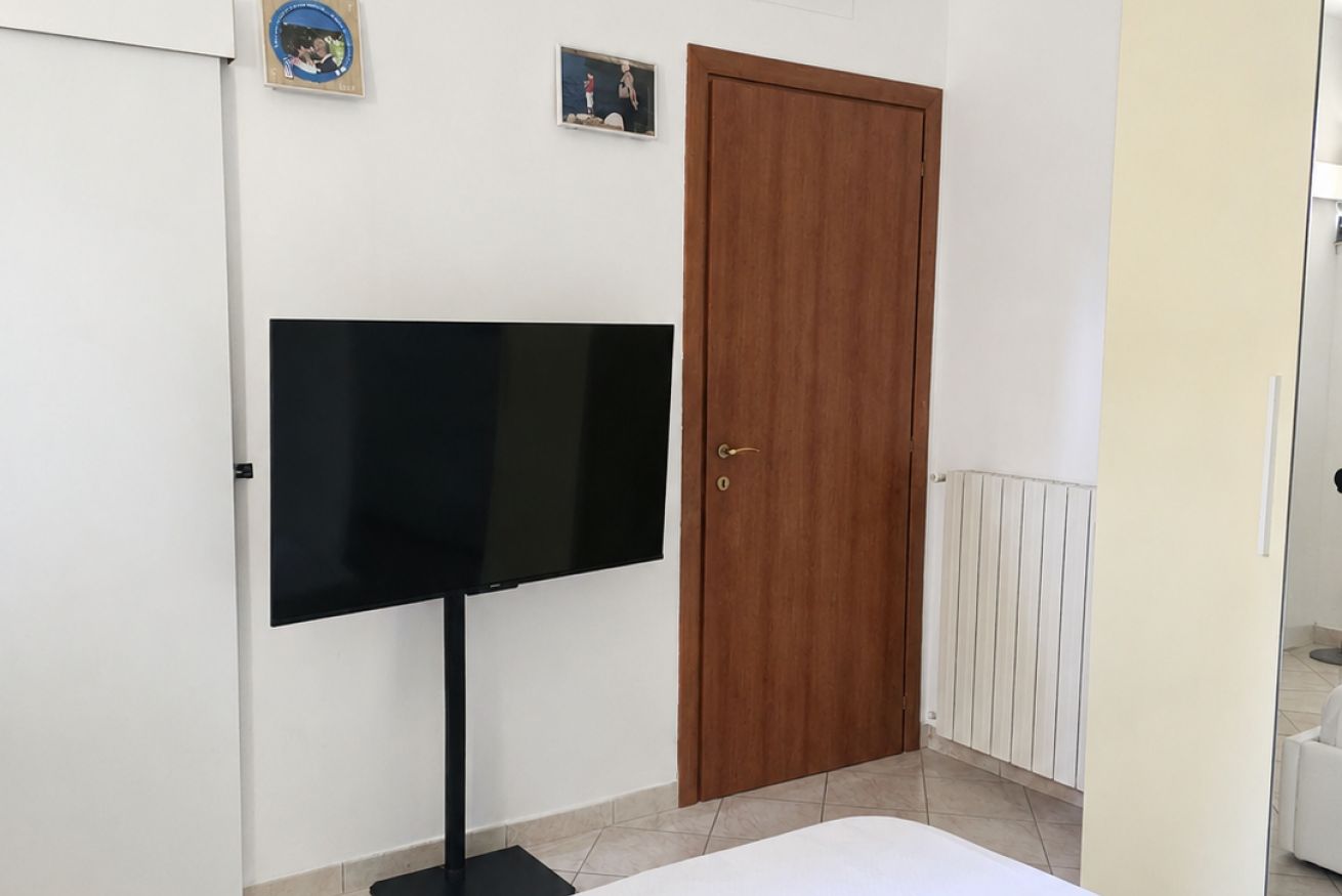 Una habitación con una televisión sobre un mueble, una puerta de madera y un radiador.