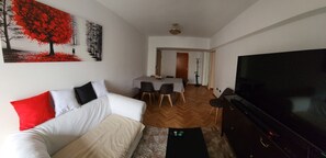 Ein Wohnzimmer mit einer Couch, einem Fernseher und einem Essbereich mit Stühlen und einem Tisch.