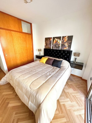 A bedroom with a bed, a wooden wardrobe, a nightstand, a wall-mounted lamp, and a painting. - Three bedrooms with parking and security. (Buenos Aires)