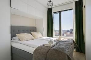 A modern hotel room with a large bed, a view of the city through the window, and a cityscape visible outside.