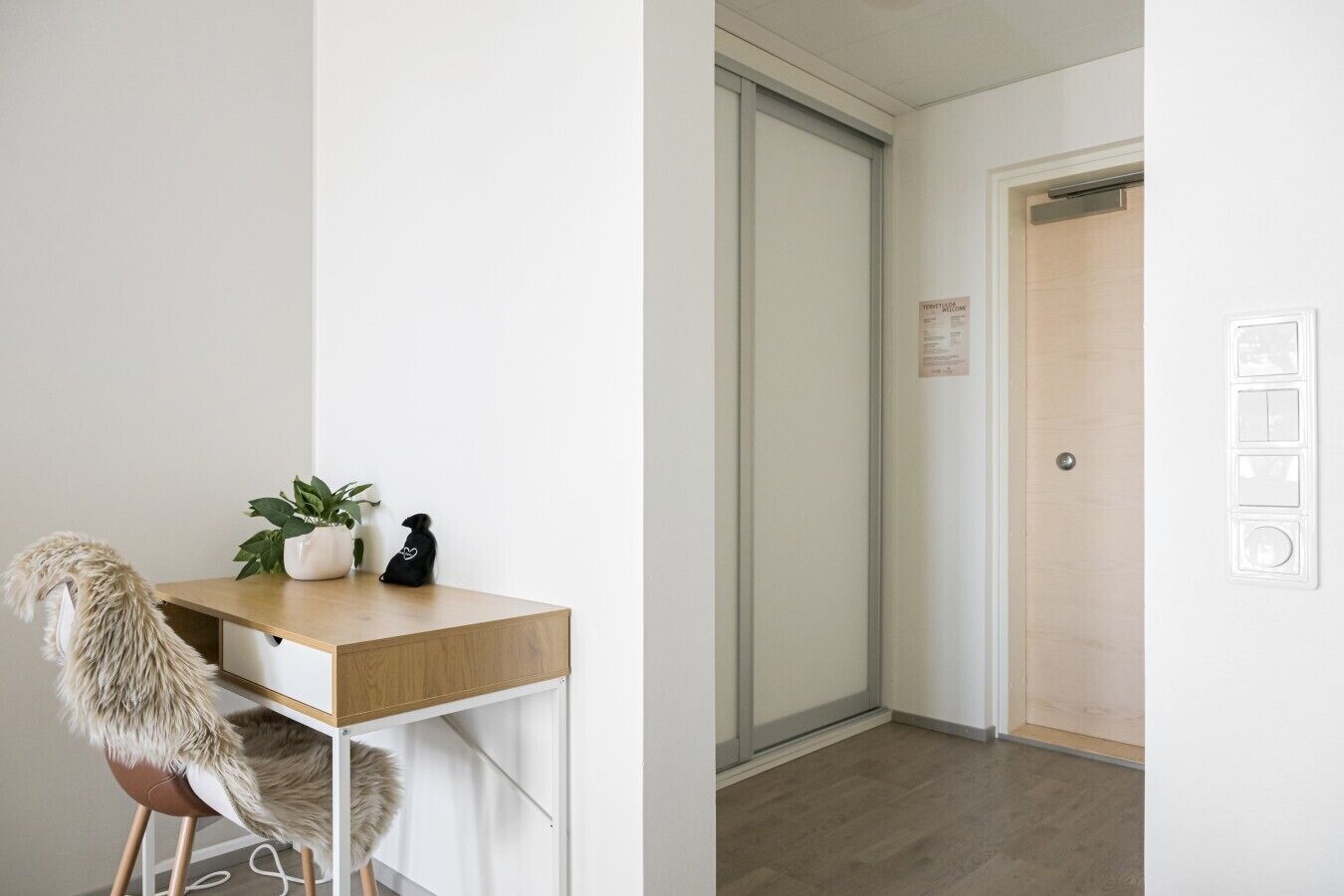 A room with a wooden desk, a chair, a potted plant, and a door with a sign.