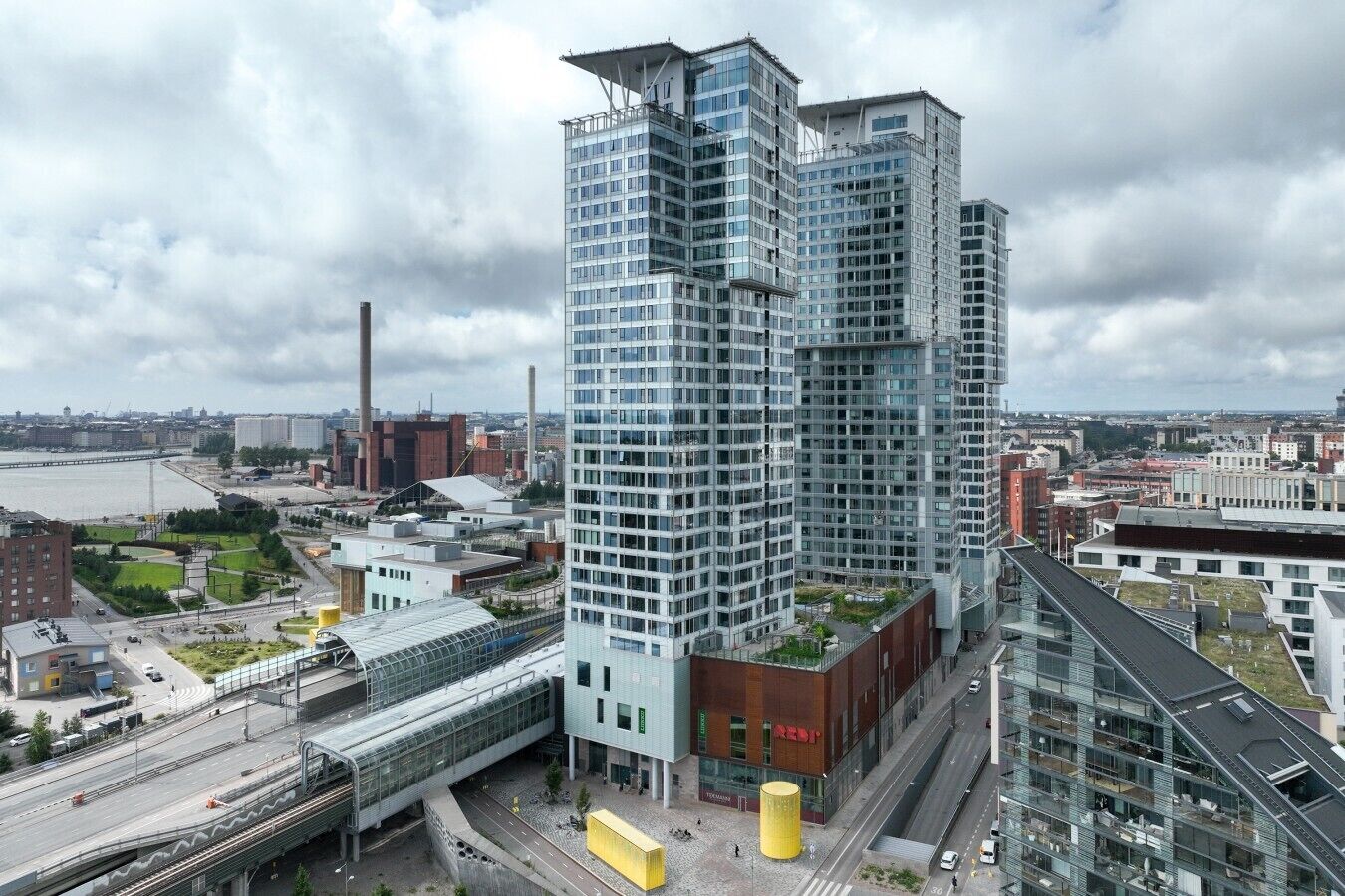 En høj bygning med en moderne glasfacade, omgivet af andre bygninger og en flod.