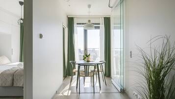 Habitación de hotel moderna con balcón, zona de comedor con mesa y sillas, y cama con cortina verde.
