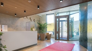 A reception area with a reception desk, seating, a red carpet, and a glass door leading outside. - Kalasatama apartments by Come in (Helsinki)
