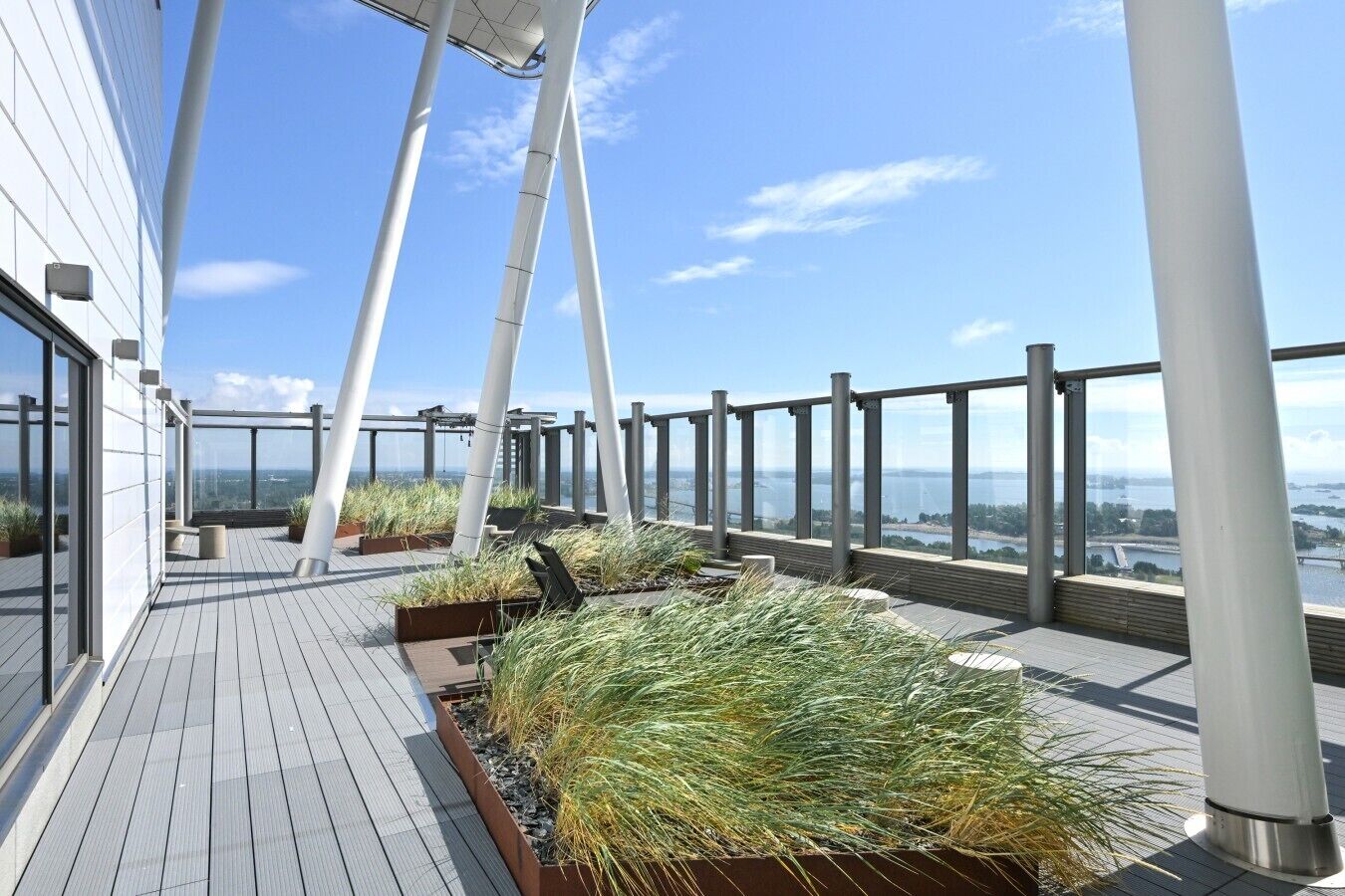 A rooftop terrace with a view of the city, featuring a wooden deck, metal railings, and potted plants.