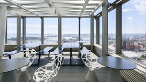 A rooftop terrace with tables and chairs, large windows offering a city view. - Kalasatama apartments by Come in (Helsinki)