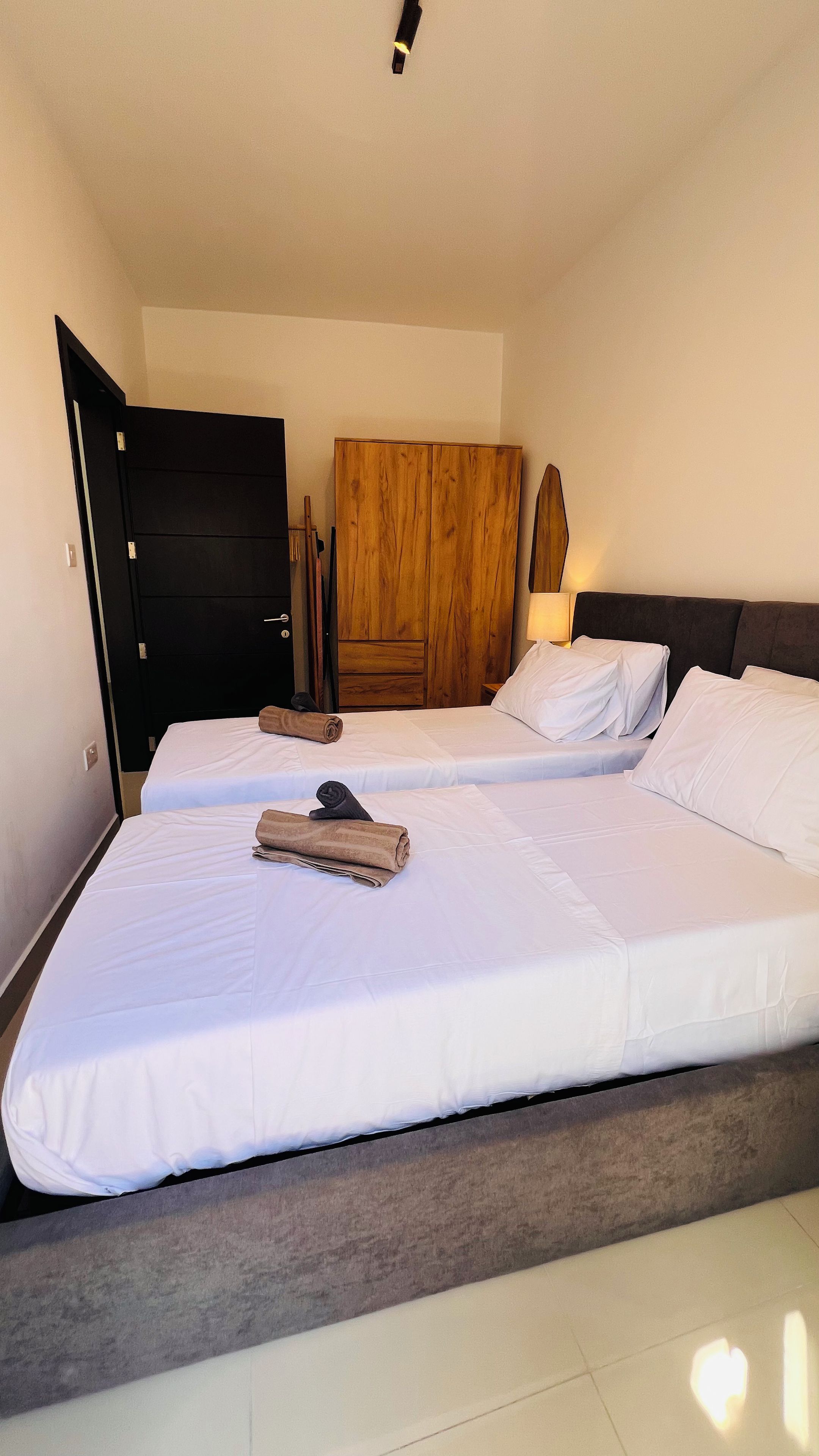 Una habitación de hotel con dos camas, un armario de madera, una mesita de noche y otra mesa auxiliar.