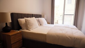 Et hotelværelse med en seng, et natbord, en lampe og et vindue med gardiner.