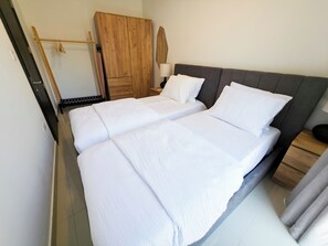 Ein Doppelbett mit weißer Bettwäsche, ein Holzschrank, ein Nachttisch mit Lampe sowie ein Spiegel an der Wand.