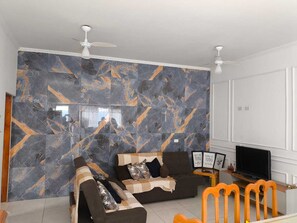 Een woonkamer met een bank, een televisie en een muur met een marmeren patroon.