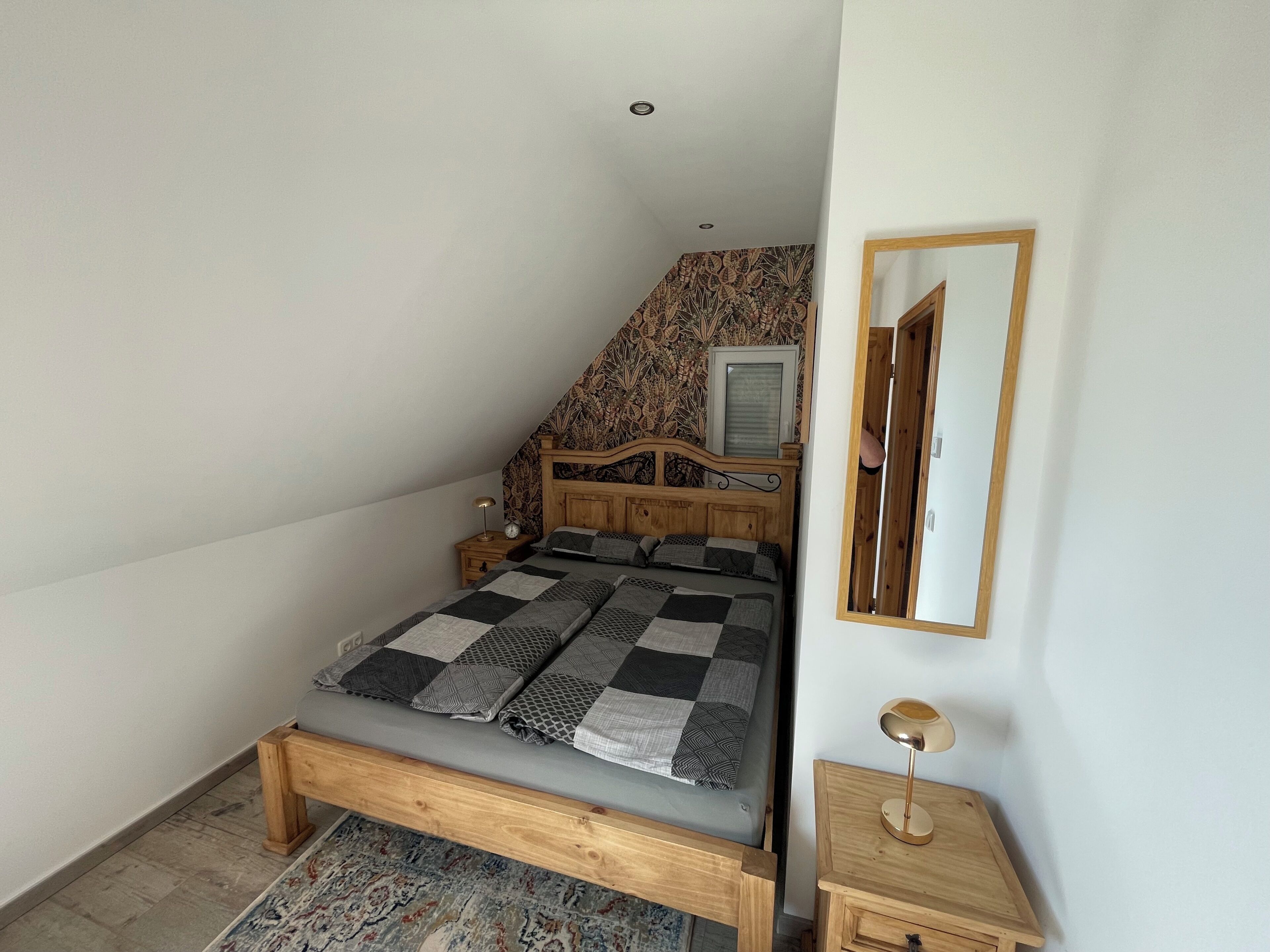 A bedroom with a wooden bed, a nightstand, a mirror, and a patterned wall.