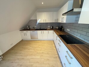 A modern kitchen with white cabinets, a wooden countertop, and a black stove. - Ferienwohnung für bis zu 6 Personen in Plattenburg (Plattenburg)