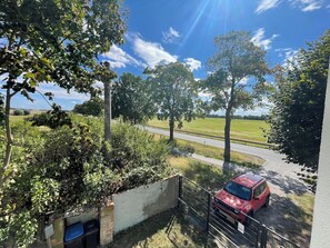 A red car parked beside a road with a white wall and a metal fence in the foreground. - Ferienwohnung für bis zu 6 Personen in Plattenburg (Plattenburg)