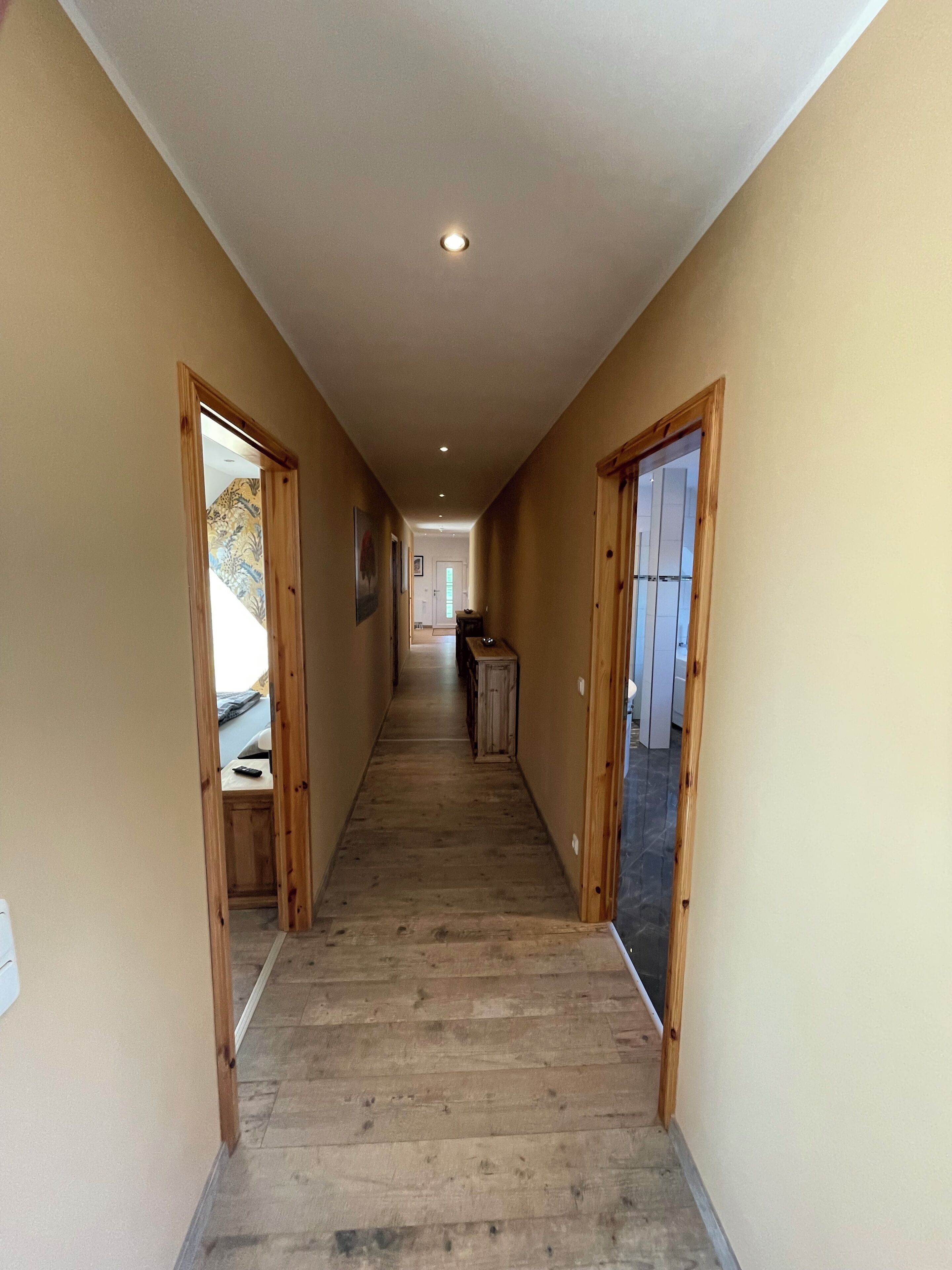A hallway with wooden flooring, beige walls, and wooden-framed doors.