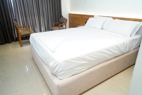 A hotel room with a large bed, a wooden headboard, a chair, and a curtain.