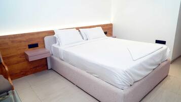 Una cama bien hecha con sábanas blancas en una habitación con cabecera de madera y una mesita de noche pequeña.