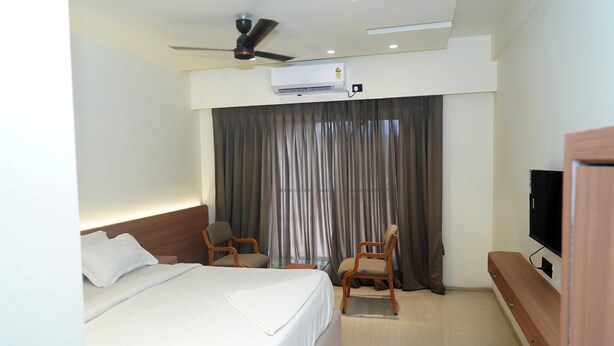 A hotel room with a bed, two chairs, a television, and an air conditioning unit.