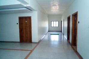 A corridor with a wooden door, a window, and a green mat on the floor.