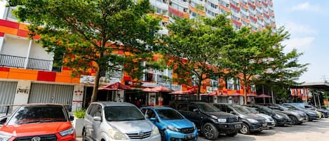Un parking rempli de voitures, un immeuble à plusieurs étages doté de balcons et des arbres.