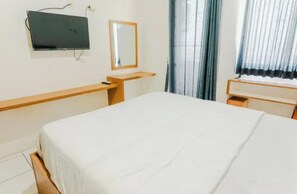 A hotel room with a bed, a desk, a chair, a television mounted on the wall, and a window with curtains. - Apartment Mahakam by Buka Kamar (Bekasi / Jawa Barat)