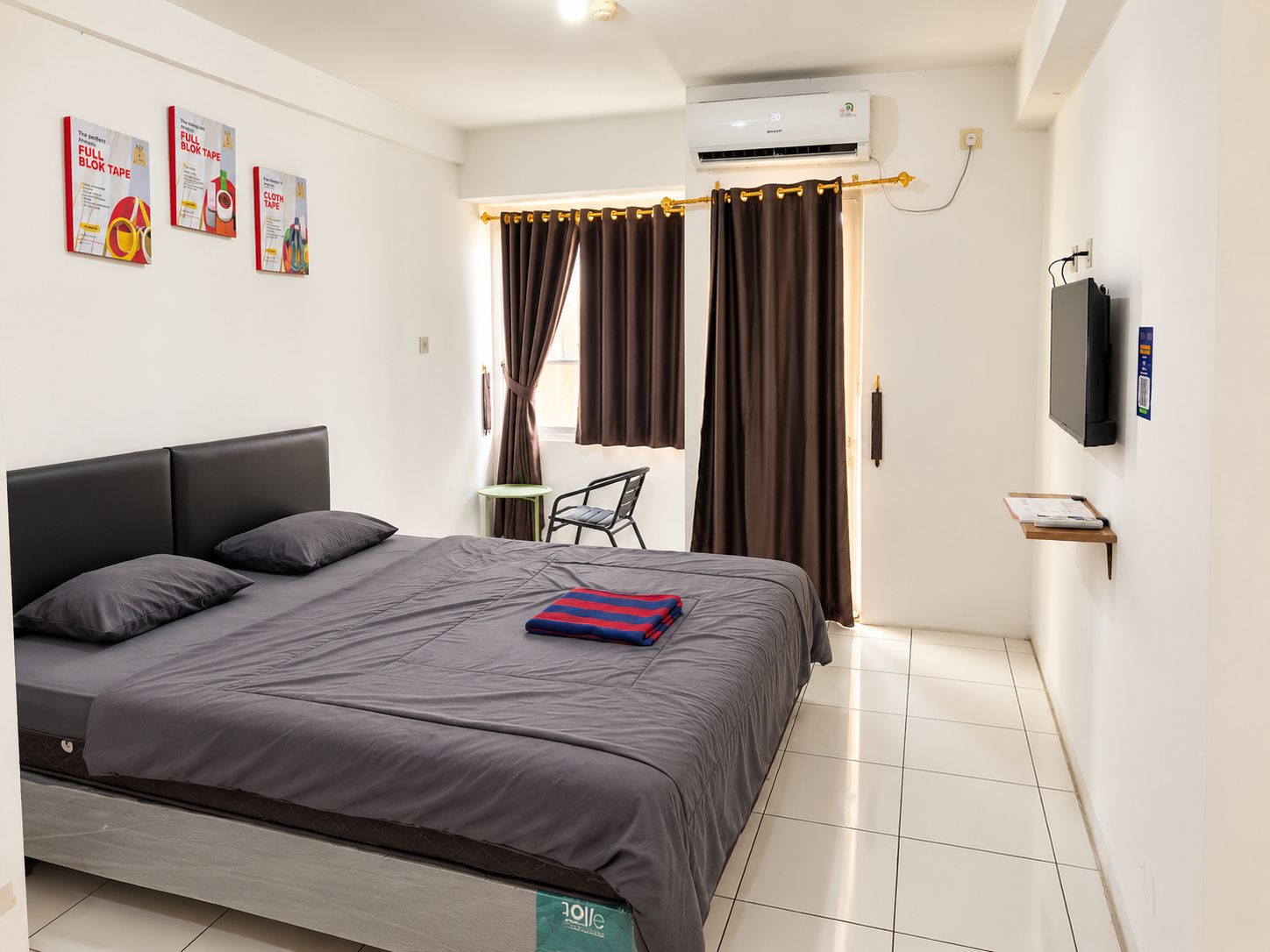 A hotel room with a bed, a chair, an air conditioning unit, and a television.