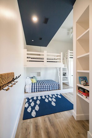 Une chambre avec un lit superposé, un tapis bleu, des murs blancs et une bibliothèque.