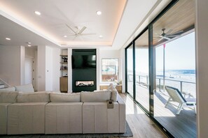 A modern living room with a large sofa, a flat-screen TV, and a balcony with a view of the beach. - Gulf Front with Panoramic Views & Elevator- Da Beach by Royal Destinations (Santa Rosa Beach)