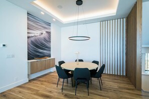 Un espace repas moderne avec une table ronde, des chaises, une suspension, une étagère murale et un grand tableau abstrait.