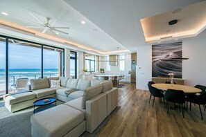 A modern living room with a large sofa, a dining area, and a view of the ocean. - Gulf Front with Panoramic Views & Elevator- Da Beach by Royal Destinations (Santa Rosa Beach)
