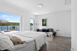 A bedroom with a large window overlooking a lake, a balcony with a grill, and a cozy bed setup. - Lakeside cabin on its own peninsula—completely secluded (hällefors)